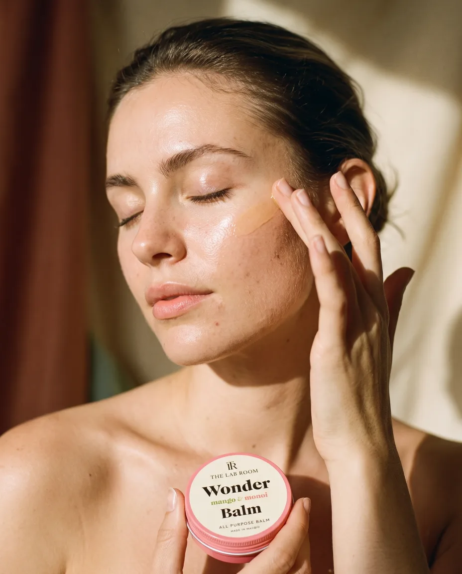 Woman with eyes closed smoothing the balm over her cheekbone, tin in hand